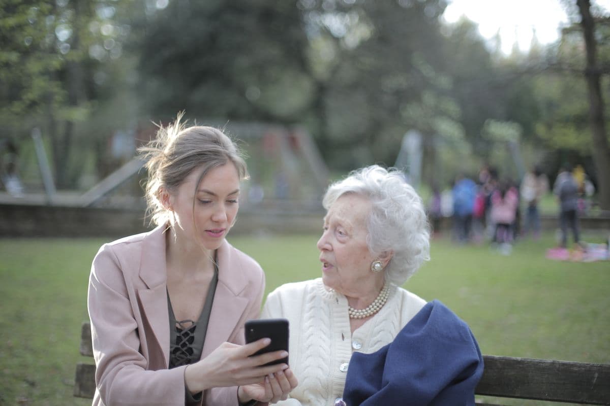 A younger woman helping an older woman with a phone on a park bench