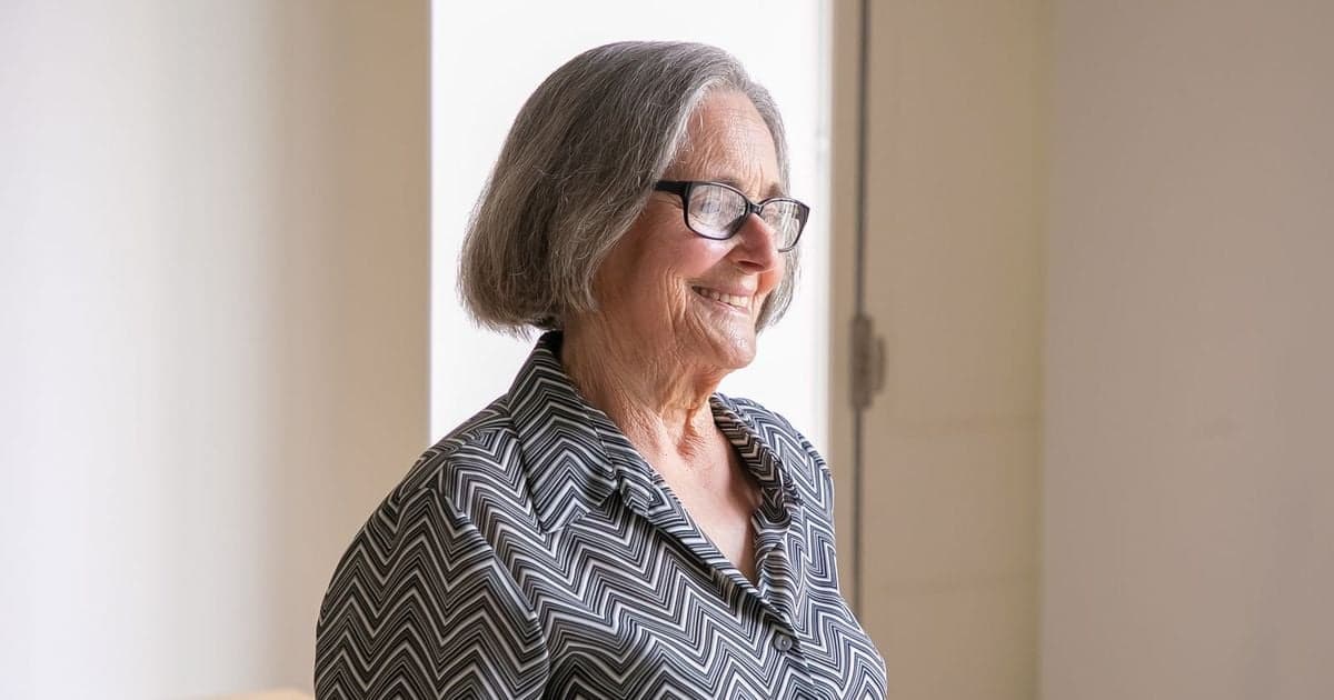 An older woman smiling by a sunlit window