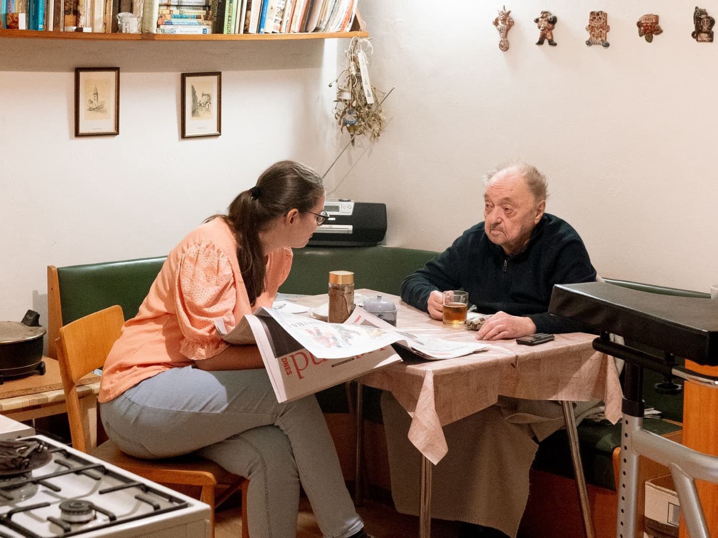 A caregiver sitting at a table with an older man, reading the paper together